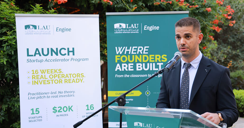 Dr. Evan Fakhoury speaking at a podium with banners in the background promoting the LAU Engine Launch Startup Accelerator Program at the Lebanese American University.