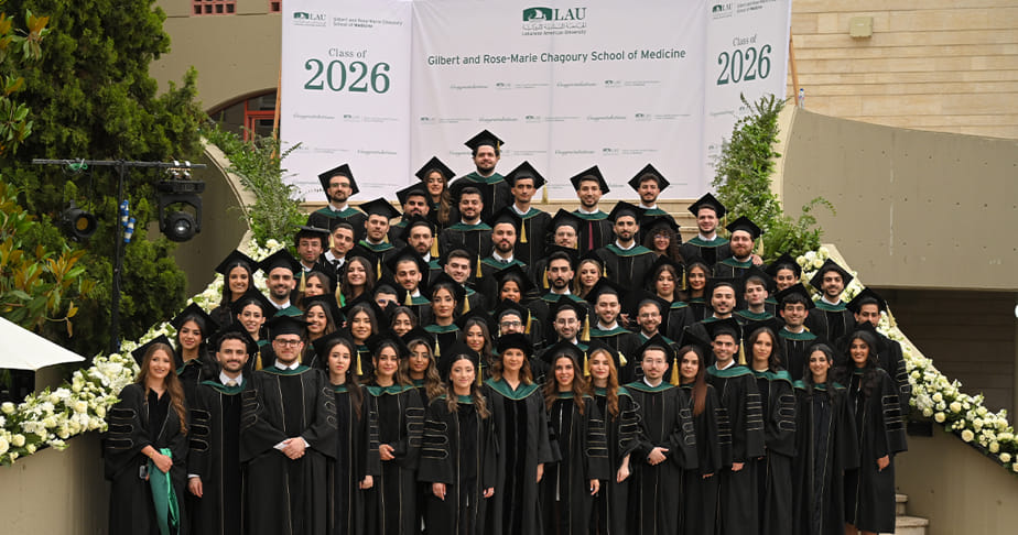 Group of graduating pharmacy students wearing caps and gowns posing for a class photo in front of a banner that reads "Gilbert and Rose-Marie Chagoury School of Medicine, Class of 2026" at the Lebanese American University.