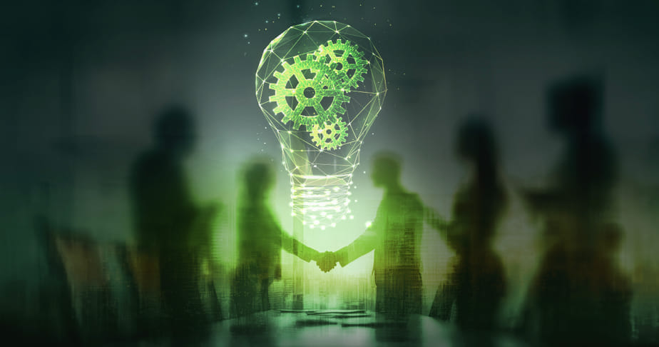 Silhouettes of people shaking hands under a glowing digital light bulb with green gears inside, symbolizing teamwork and innovation.