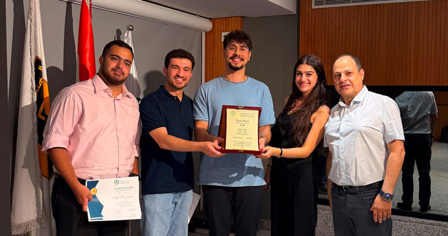 A team of engineering students standing indoors, with two of them holding a certificate and a plaque.