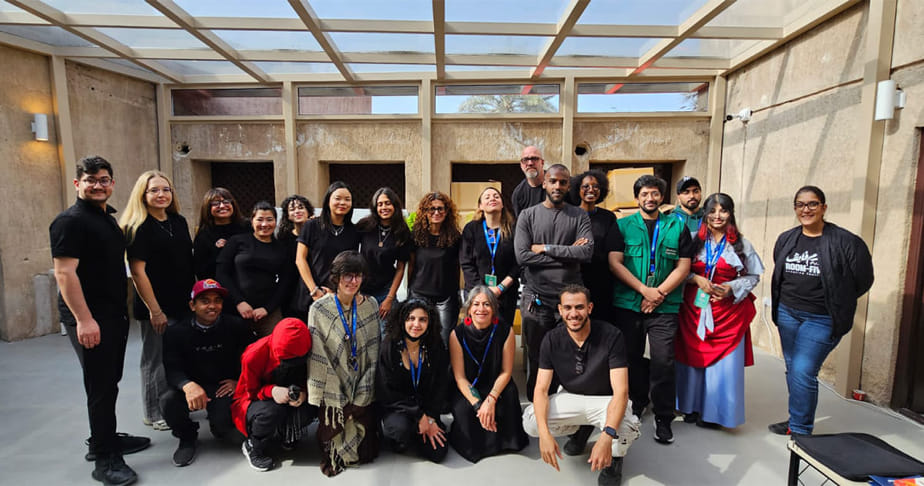 Group of diverse people posing together indoors with a windowed ceiling and beige walls.