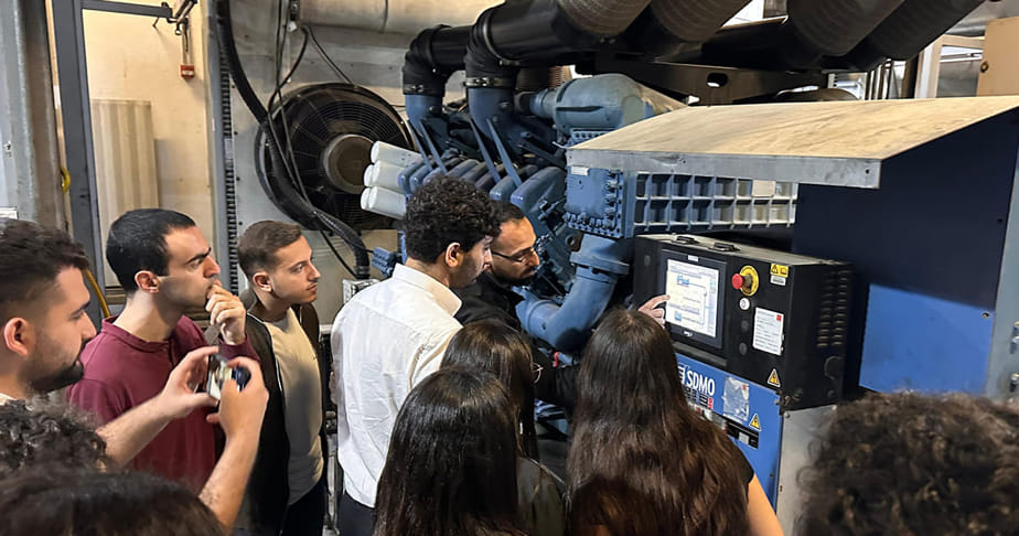 A group of people observing and discussing a large industrial machine with a control panel in a factory setting.